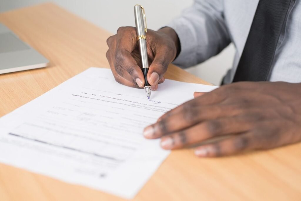 Hands signing a power of attorney document with a pen on a wooden desk