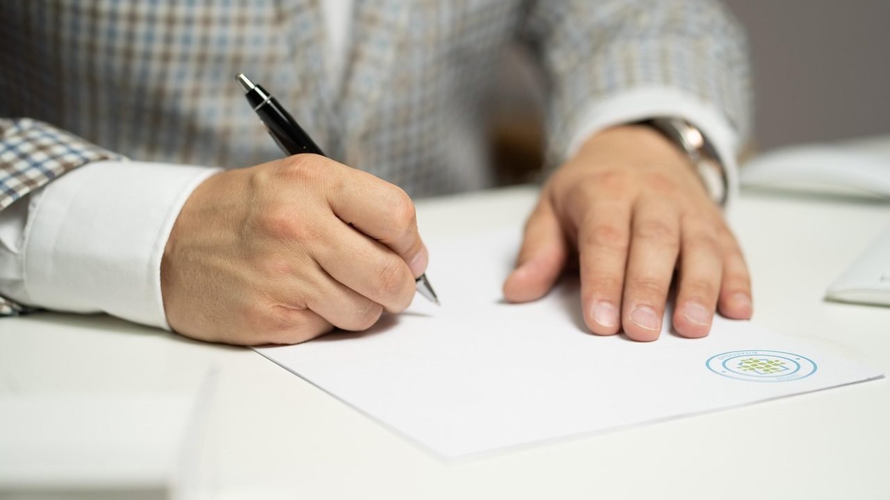 رجل يوقع بقلم حبر على ورقة بيضاء فوق مكتب في مكتب عمل