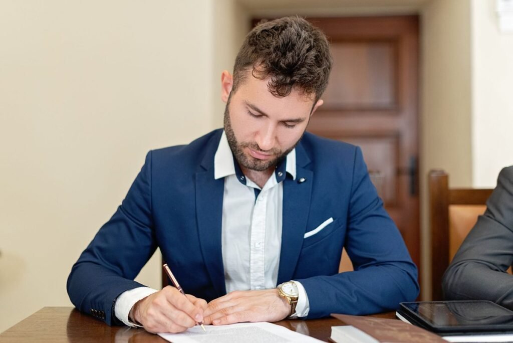Man in a blue suit signing papers at an office desk before a power of attorney to close a bank account