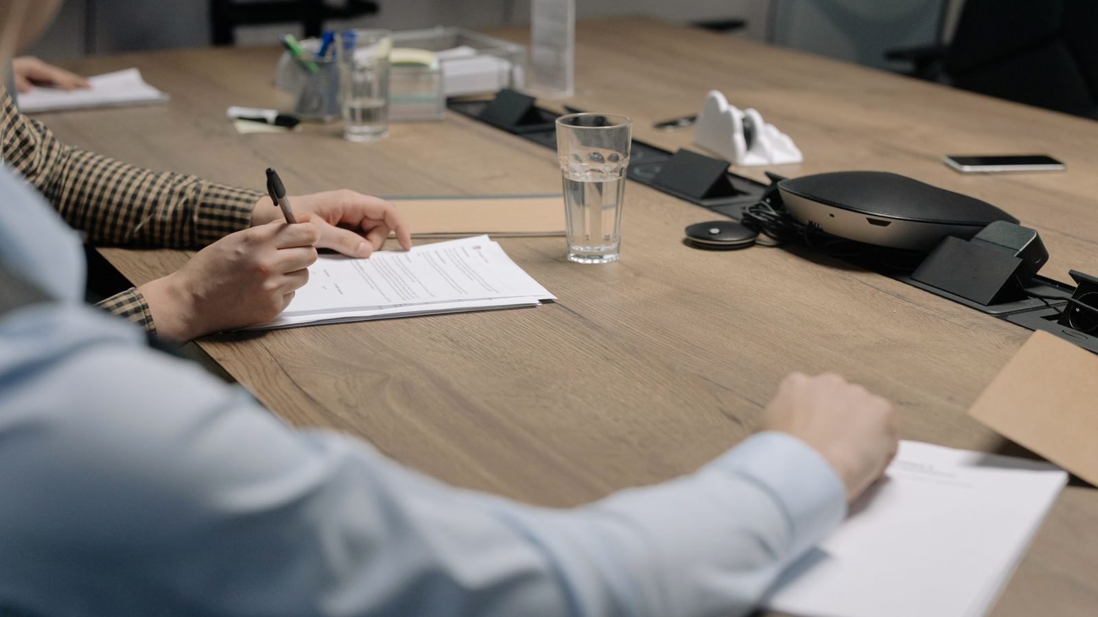 Two people signing papers at a wooden meeting table, preparing a power of attorney for credit card