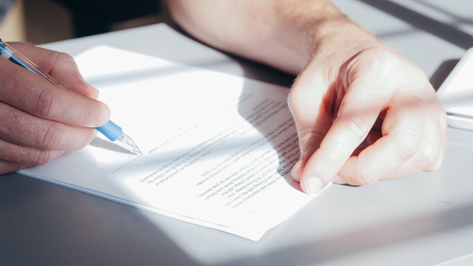 Hands signing a document to notarize family POA in Dubai, blue pen on a desk
